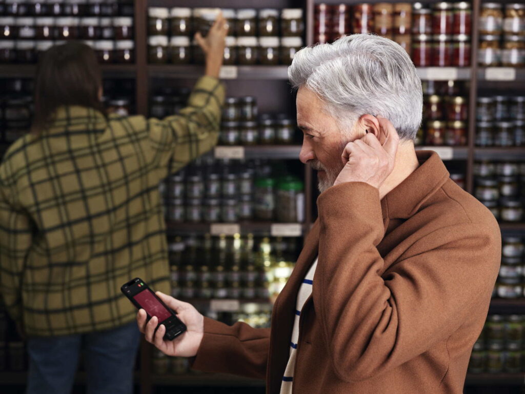 Stariji čovek koji nosi pametne slušne aparate u prodavnici.
